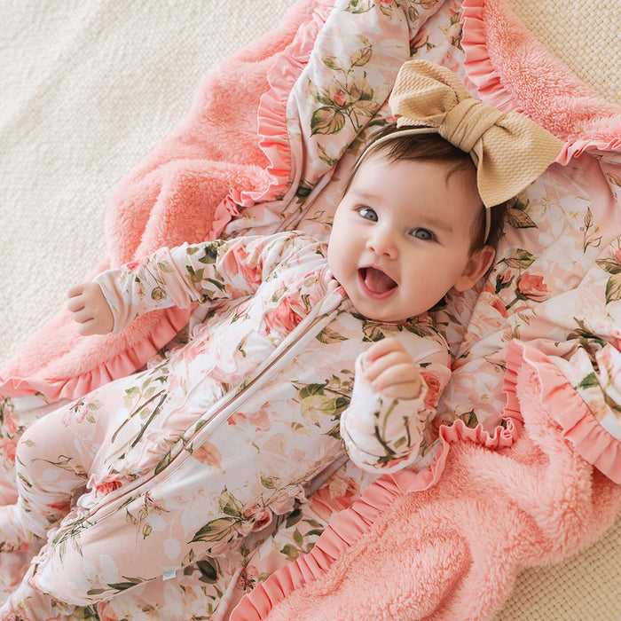 Baby in a floral outfit with a large bow laying on a matching pink floral blanket.